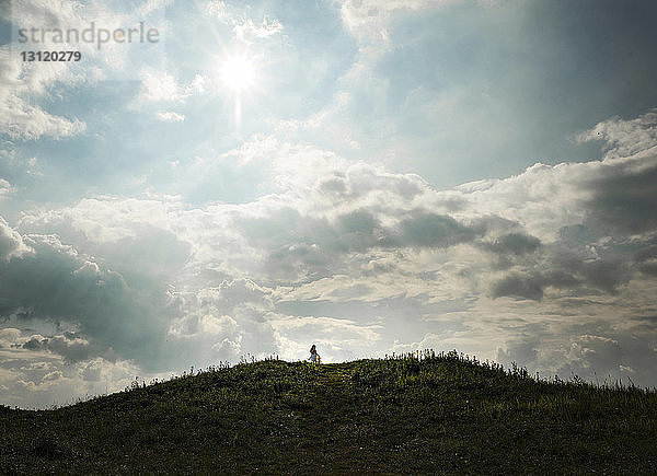Mitteldistanzansicht eines Mädchens  das auf einem Hügel vor bewölktem Himmel steht