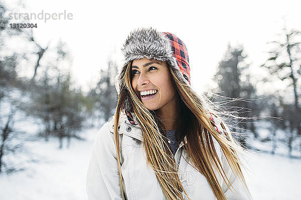 Nahaufnahme einer fröhlichen Frau mit Pelzmütze  die auf einem schneebedeckten Feld steht