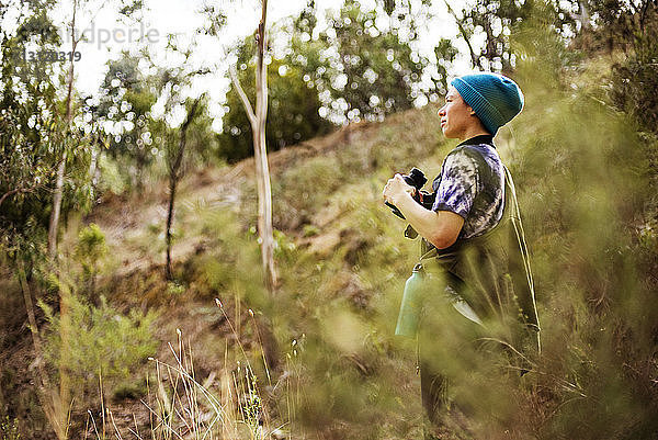 Seitenansicht einer Frau  die mit einem Fernglas in der Hand im Wald wegschaut