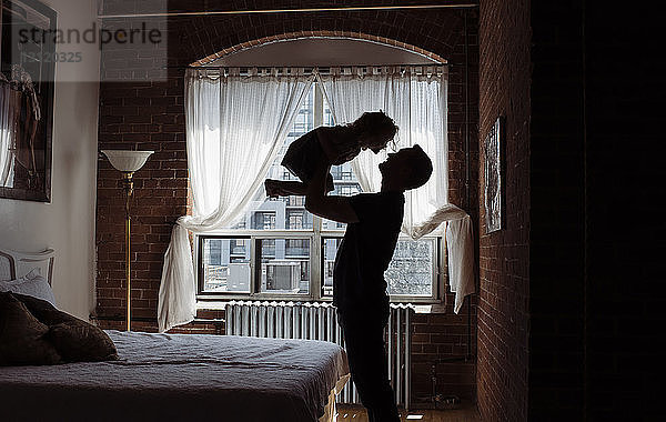 Silhouettenvater holt Tochter ab  während er zu Hause am Bett steht