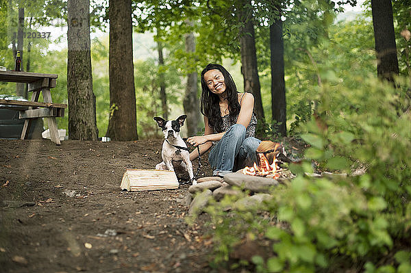 Porträt einer glücklichen Frau  die mit einem Boston Terrier im Wald sitzt
