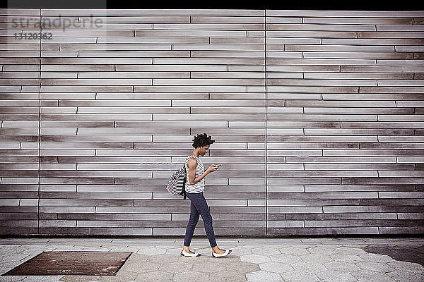 Seitenansicht einer Frau  die ein Smartphone benutzt  während sie gegen eine Wand läuft