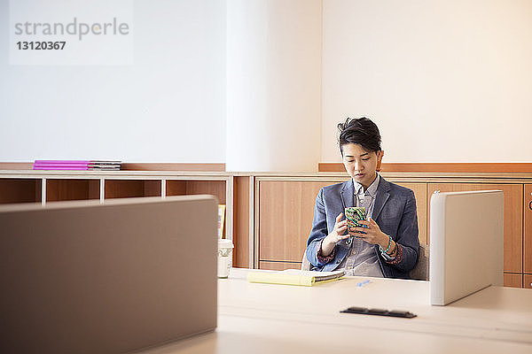 Zuversichtliche Geschäftsfrau benutzt Mobiltelefon am Tisch im Büro