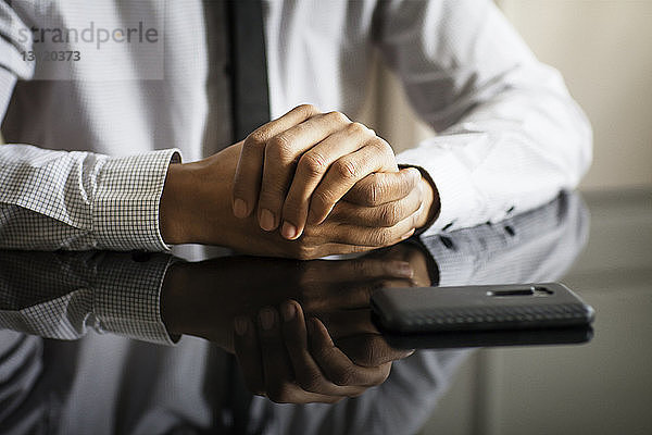 Mittelteil eines Geschäftsmannes mit gefalteten Händen am Tisch sitzend im Büro