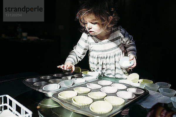 Süßes Mädchen ordnet Cupcake-Halter im Backblech an