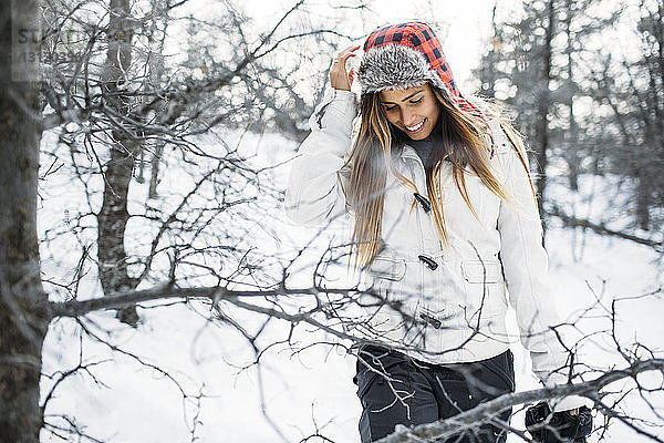 Frontansicht einer lächelnden Frau mit Pelzmütze  die auf einem schneebedeckten Feld steht