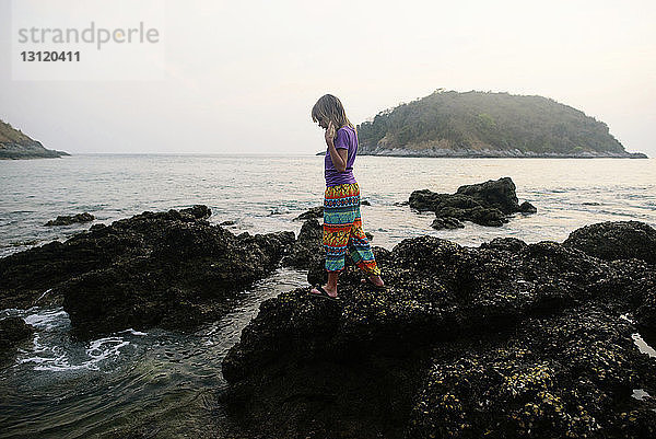 Seitenansicht eines am Ufer auf Felsen stehenden Mädchens