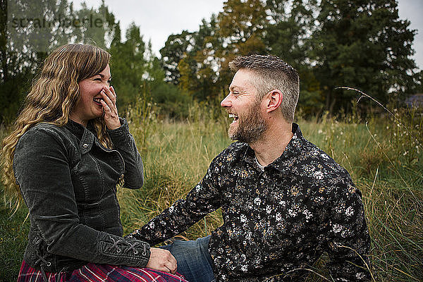 Glückliches Paar sieht sich an  während es auf einem Grasfeld auf einem Bauernhof sitzt