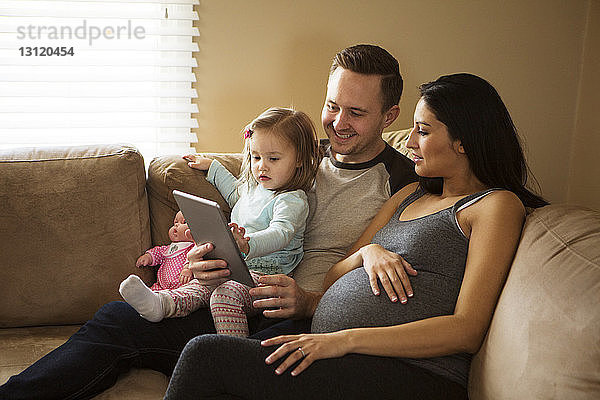 Familie schaut auf Tablet-Computer  während sie zu Hause auf dem Sofa sitzt
