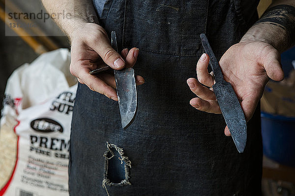 Mittelteil eines Schmiedes  der Messer hält  während er in der Werkstatt steht