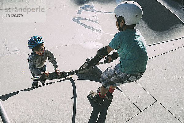 Brüder ziehen bei Sonnenschein Roller im Skateboard-Park