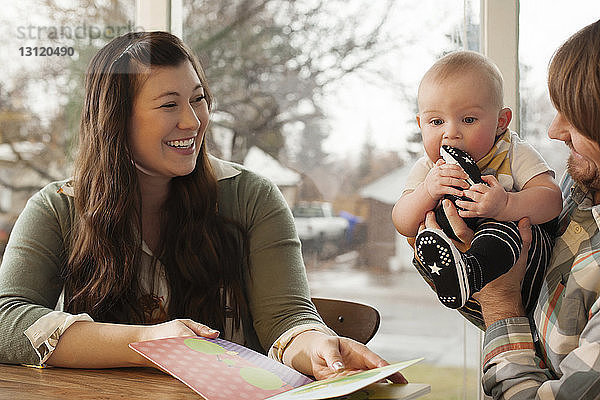 Glückliche Eltern mit Baby und Bilderbuch am heimischen Tisch