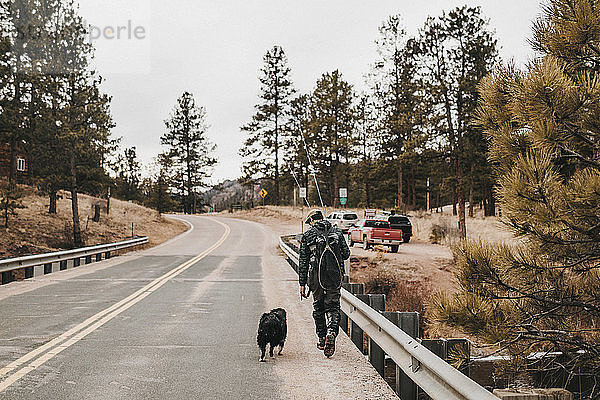 Rückansicht eines männlichen Wanderers mit Hund beim Gehen auf der Straße