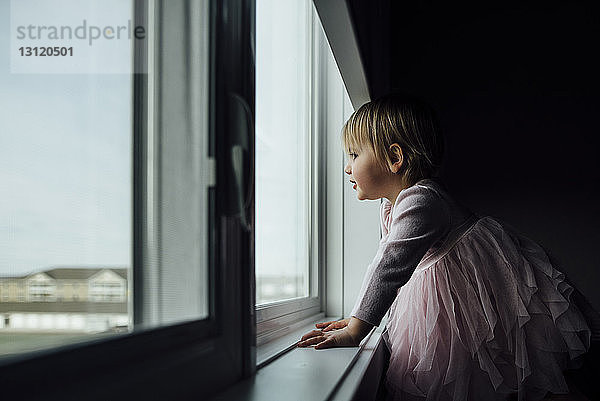 Seitenansicht eines zu Hause am Fenster stehenden Mädchens