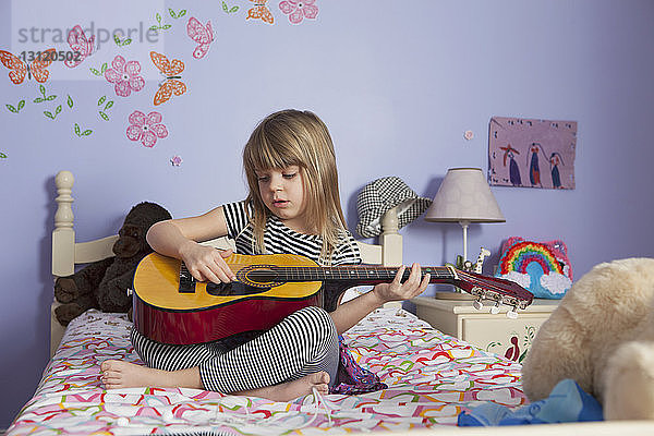 Mädchen spielt zu Hause im Bett Gitarre