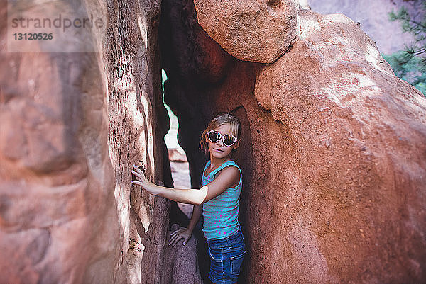 Porträt eines Mädchens mit Sonnenbrille in Herzform  das inmitten von Felsen steht
