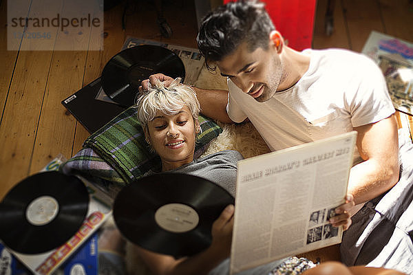 Draufsicht eines Paares  das auf dem Boden liegend auf Vinyl-Schallplatten schaut
