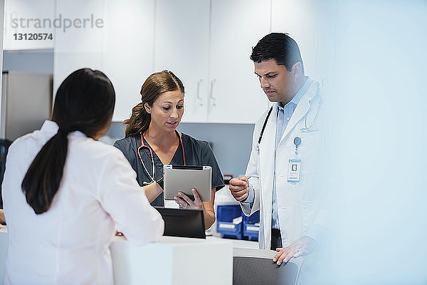 Krankenschwester zeigt einer Kollegin einen Tablet-Computer  während im Vordergrund eine Ärztin steht