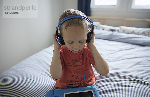 Hochwinkelansicht eines Jungen  der zu Hause auf dem Bett sitzend Musik hört