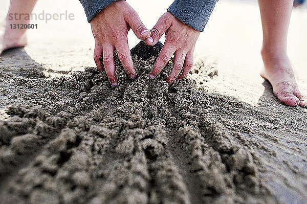 Ausgeschnittenes Bild eines Jungen  der am Strand mit Sand spielt