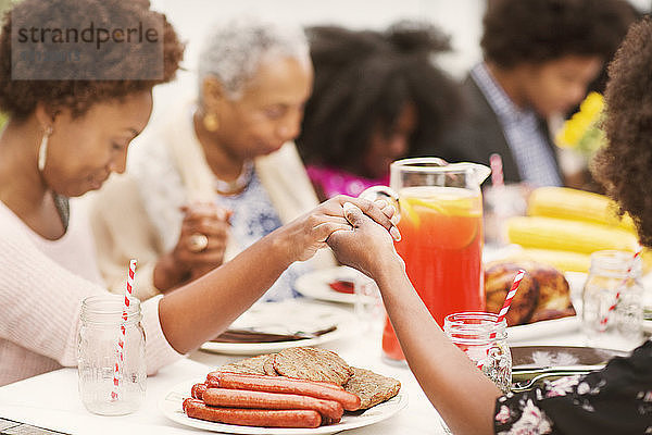 Familie hält beim Gebet am Frühstückstisch Händchen