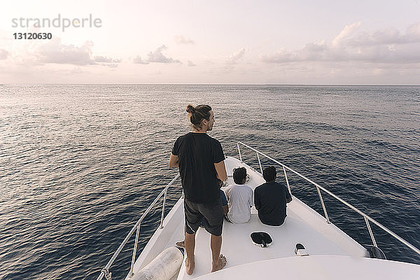 Rückansicht von männlichen Freunden  die bei Sonnenuntergang auf einer Yacht auf See gegen den Himmel reisen