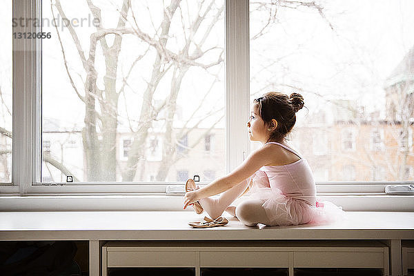 Mädchen sitzt auf Tisch und trägt Ballettschuhe gegen Fenster