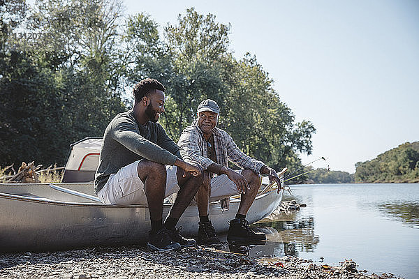 Männliche Freunde unterhalten sich auf einem Boot am Seeufer bei klarem Himmel