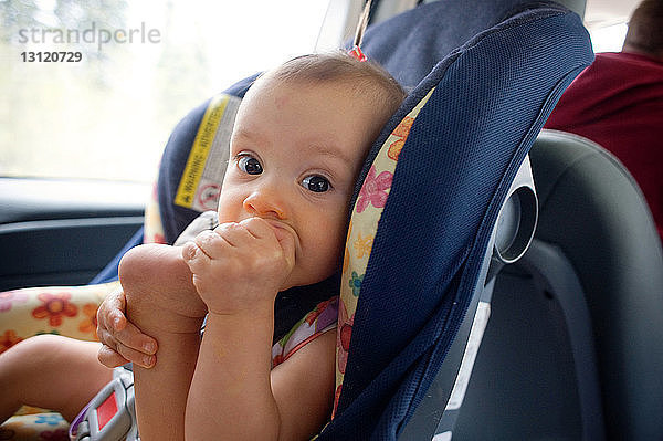 Porträt eines kleinen Mädchens  das in den Fuß beißt  während es auf einem Autositz sitzt