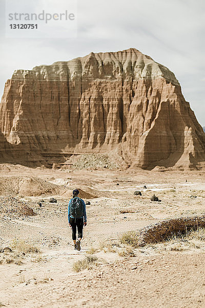 Rückansicht einer Wanderin mit Rucksack  die bei Sonnenschein die Wüste vor Felsformationen erkundet