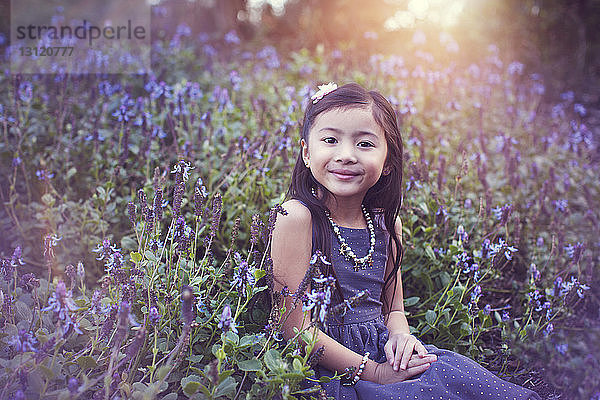 Porträt eines niedlichen Mädchens  das inmitten blühender Pflanzen im Park sitzt