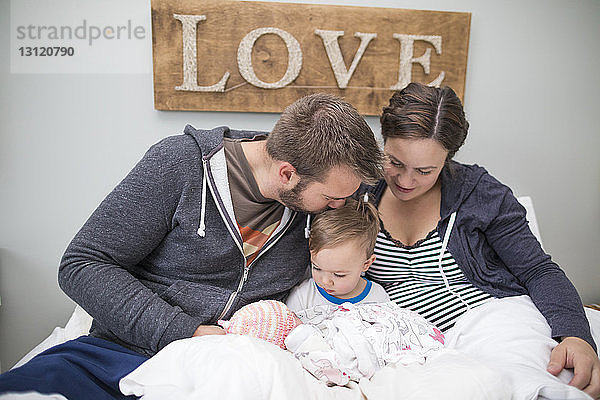 Liebevolle Eltern mit Sohn und neugeborener Tochter zu Hause im Bett sitzend