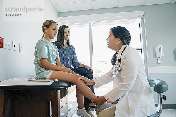 Mutter sieht Kinderarzt an  der das Kniegelenk der Tochter im medizinischen Untersuchungsraum untersucht