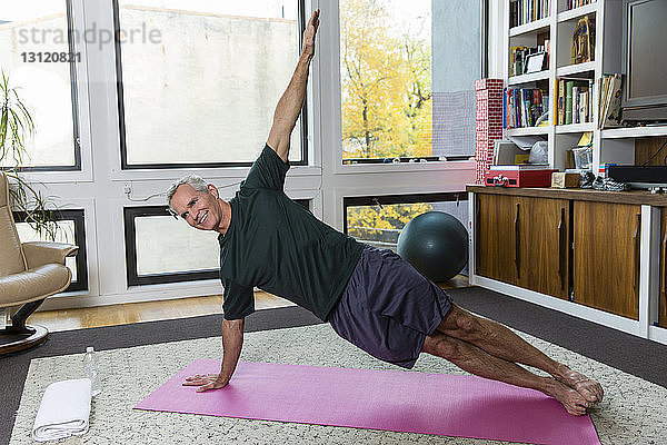 Ein reifer Mann  der zu Hause auf einer Übungsmatte Yoga praktiziert