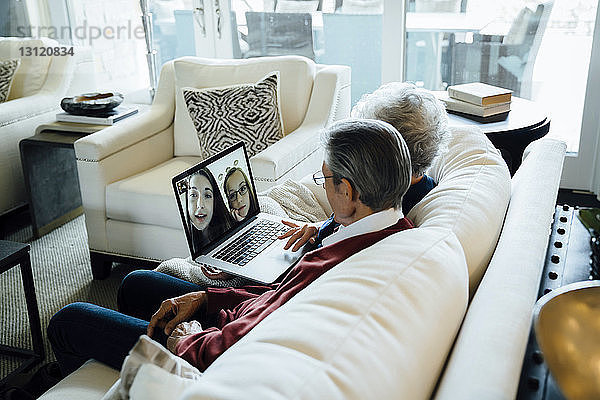 Älteres Ehepaar Videokonferenzen mit Enkelinnen über Laptop-Computer  während es auf dem Sofa im Wohnzimmer sitzt