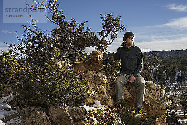 Mann mit Hund sitzt auf Felsformationen gegen den Himmel im Bryce Canyon National Park