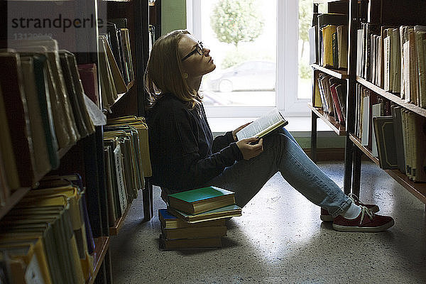 Frau hält Buch und schaut auf  während sie in der Bibliothek sitzt