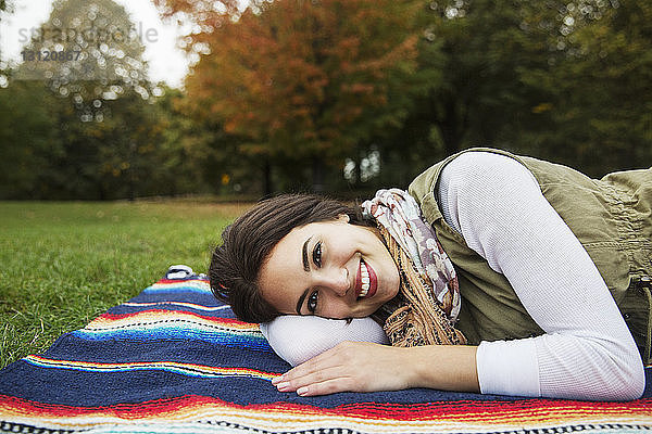 Porträt einer glücklichen Frau auf einer Decke liegend im Park