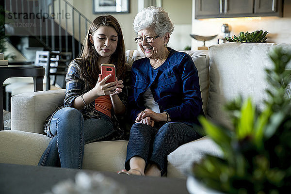 Enkelin zeigt der Großmutter ein Smartphone  während sie zu Hause auf dem Sofa sitzt