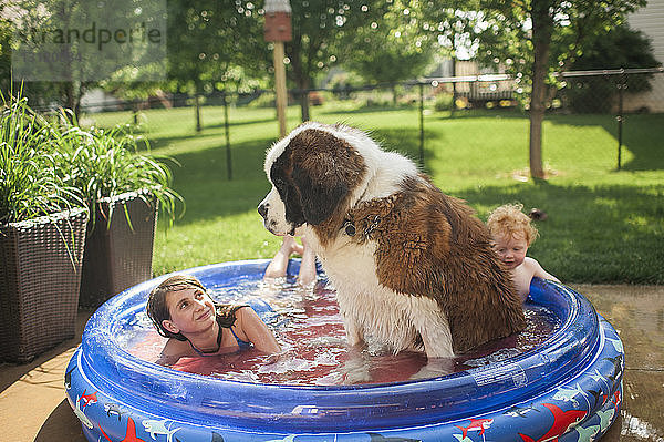 Geschwister mit Hund schwimmen im Planschbecken auf dem Hof