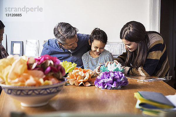 Vater und Mutter mit Töchtern  die bei Tisch Papierblumen basteln