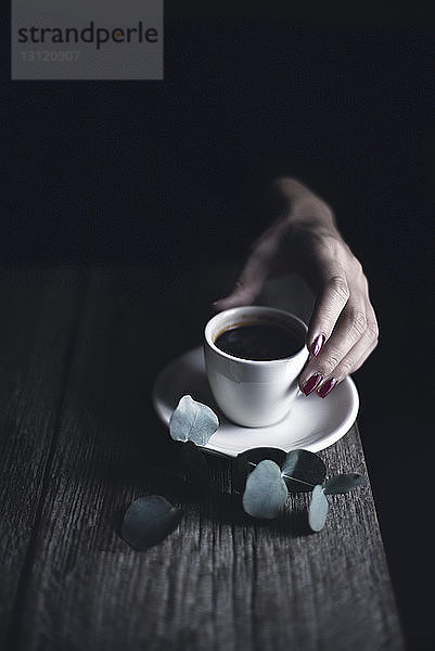Beschnittenes Bild einer Frau  die in der Dunkelkammer eine Kaffeetasse am Tisch hält