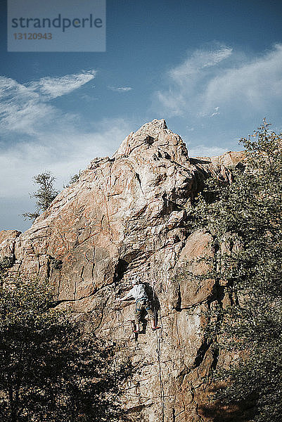 Niedrigwinkelansicht eines Mannes  der an einem sonnigen Tag am Fels gegen den Himmel klettert