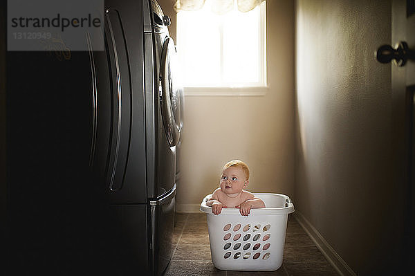 Kleiner Junge ohne Hemd im Wäschekorb  der die Waschmaschine anschaut