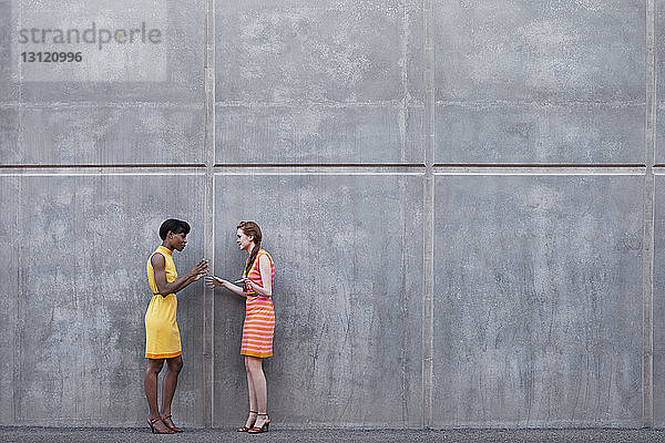 Multiethnische Freunde unterhalten sich in voller Länge  während sie an der Wand stehen