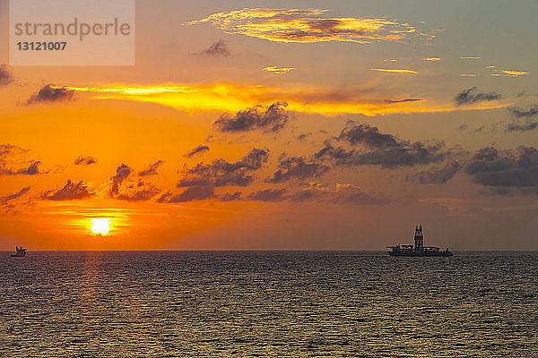 Fernansicht der Bohrinsel im Meer gegen bewölkten Himmel bei Sonnenuntergang