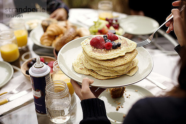 Beschnittenes Bild einer Frau  die Pfannkuchen am Frühstückstisch hält
