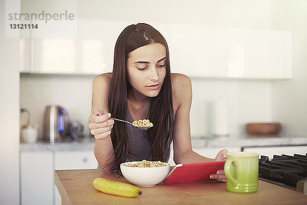 Frau benutzt digitales Tablett beim Frühstücken zu Hause auf dem Tisch