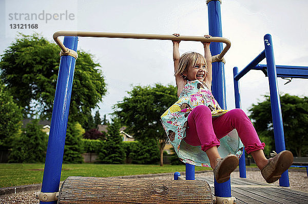 Fröhliches Mädchen hängt an Affenstangen im Park