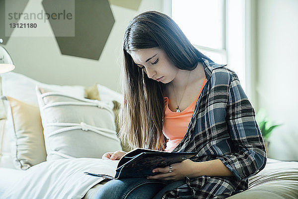 Teenager-Mädchen liest Zeitschrift  während sie im Schlafzimmer sitzt